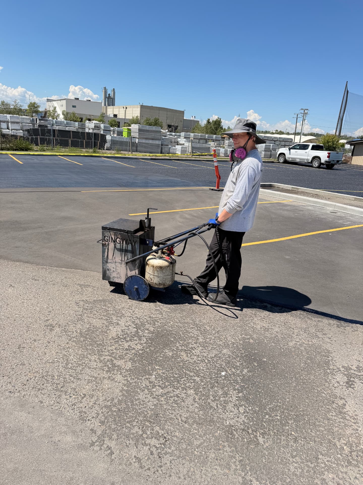 Technician operating asphalt maintenance equipment on a Calgary commercial lot